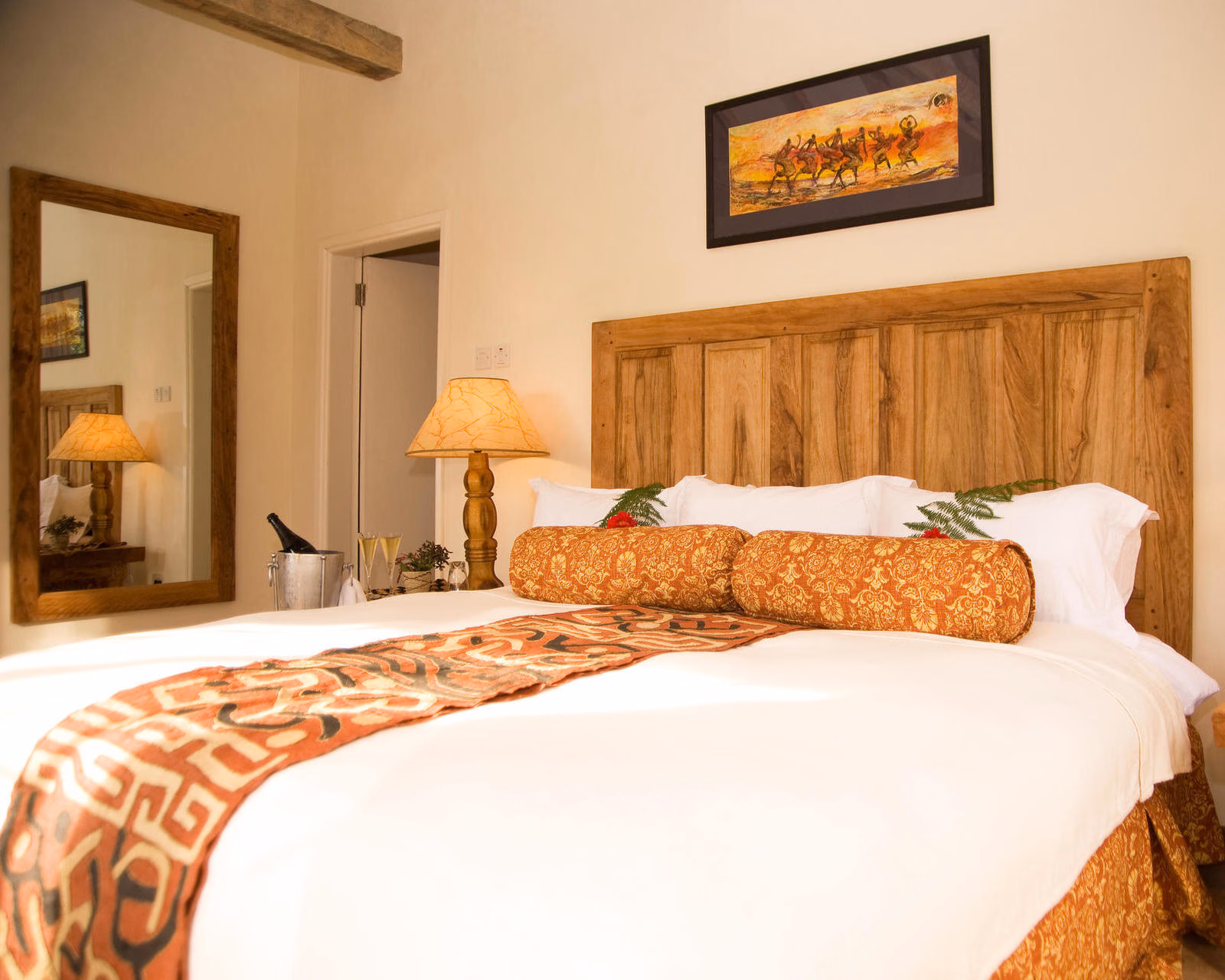 Luxurious bed at Clouds Lodge Uganda with wooden headboard, white linens, orange pillows, and a champagne bucket.