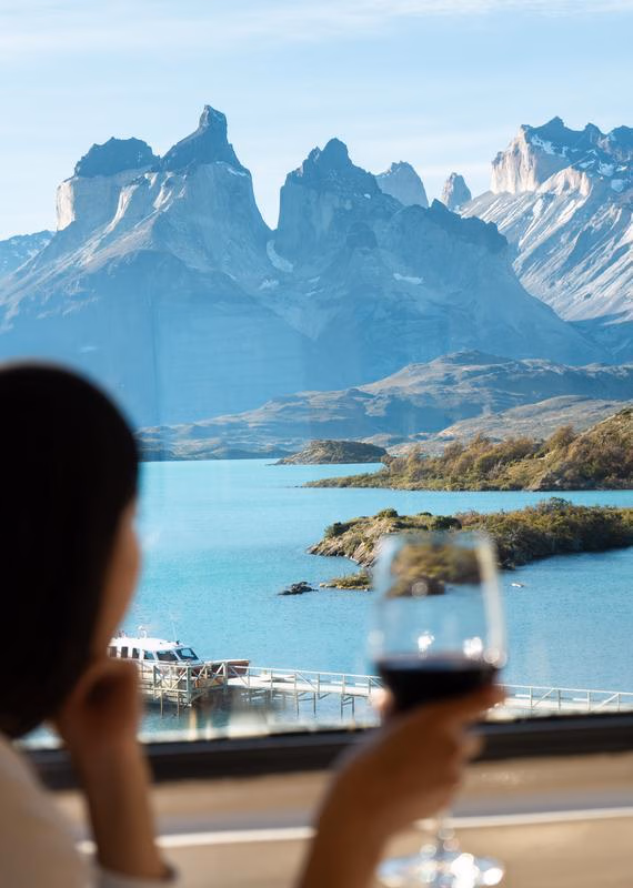 Silhouette of a person holding a wine glass while looking through an Explora Patagonia window at sharp mountains.