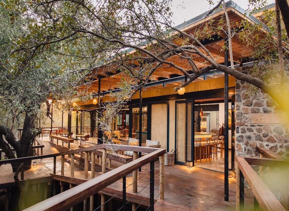 Wooden deck entrance to Jaci's Private Lodge with large trees and a stone wall reading JACI'S SAFARI LODGE.
