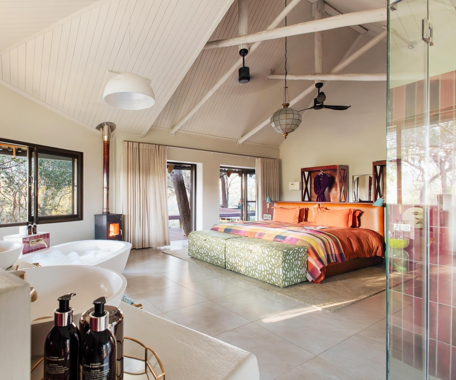 Spacious bedroom at Jaci's Private Lodge with a brightly colored bed, a white bathtub, and large scenic windows.