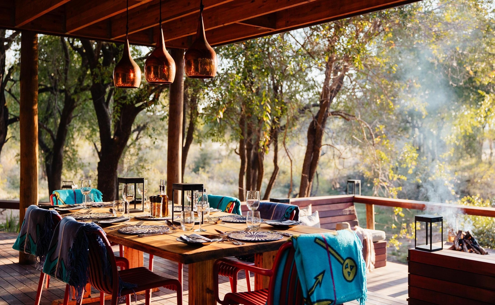 Set outdoor dining table at Jaci's Private Lodge under a wooden roof, with colorful blankets and copper lights.