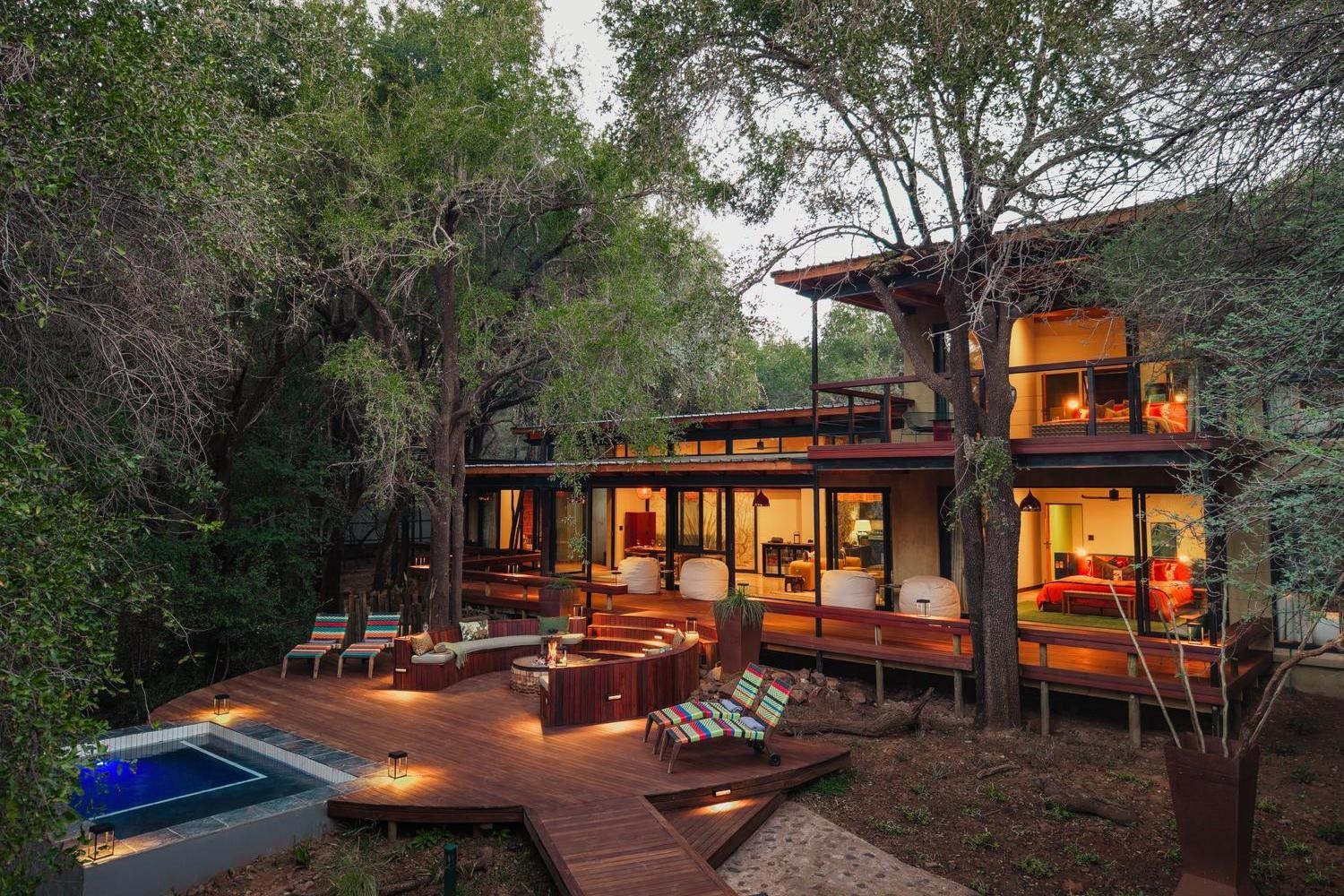 Two-story exterior of Jaci's Private Lodge at dusk, featuring wooden decks, a sunken fire pit, and a small pool.