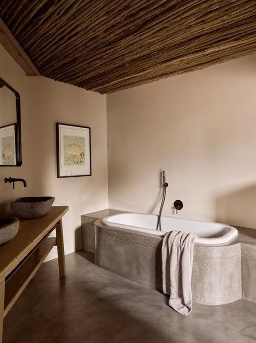 A modern luxury bathroom with a bathtub, wooden vanity, stone sinks, and a stick ceiling.