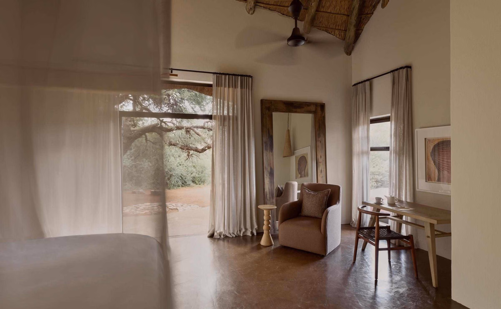 An interior bedroom view showing a cozy armchair, writing desk, and open door framed by light curtains.
