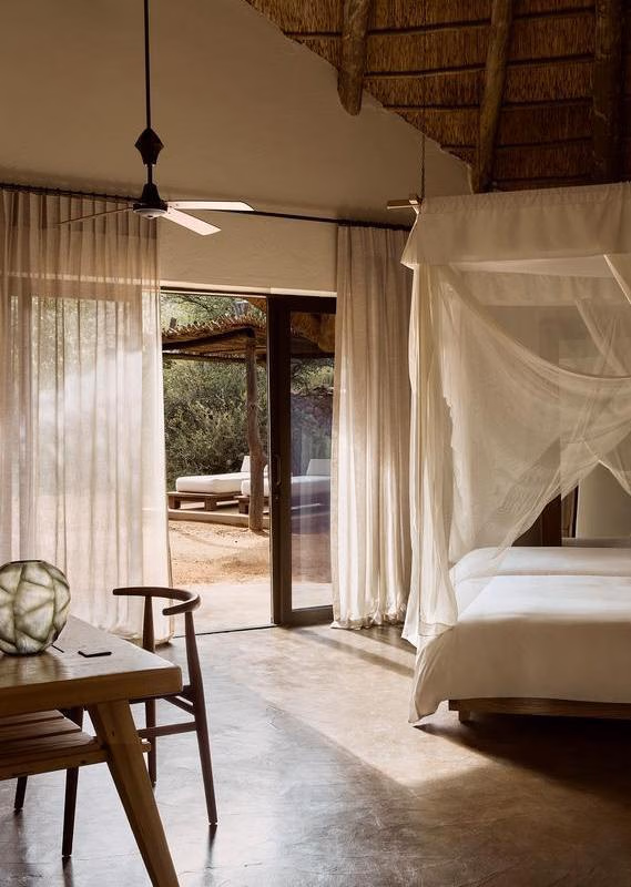 A modern lodge bedroom featuring a netted canopy bed and glass doors leading outside.