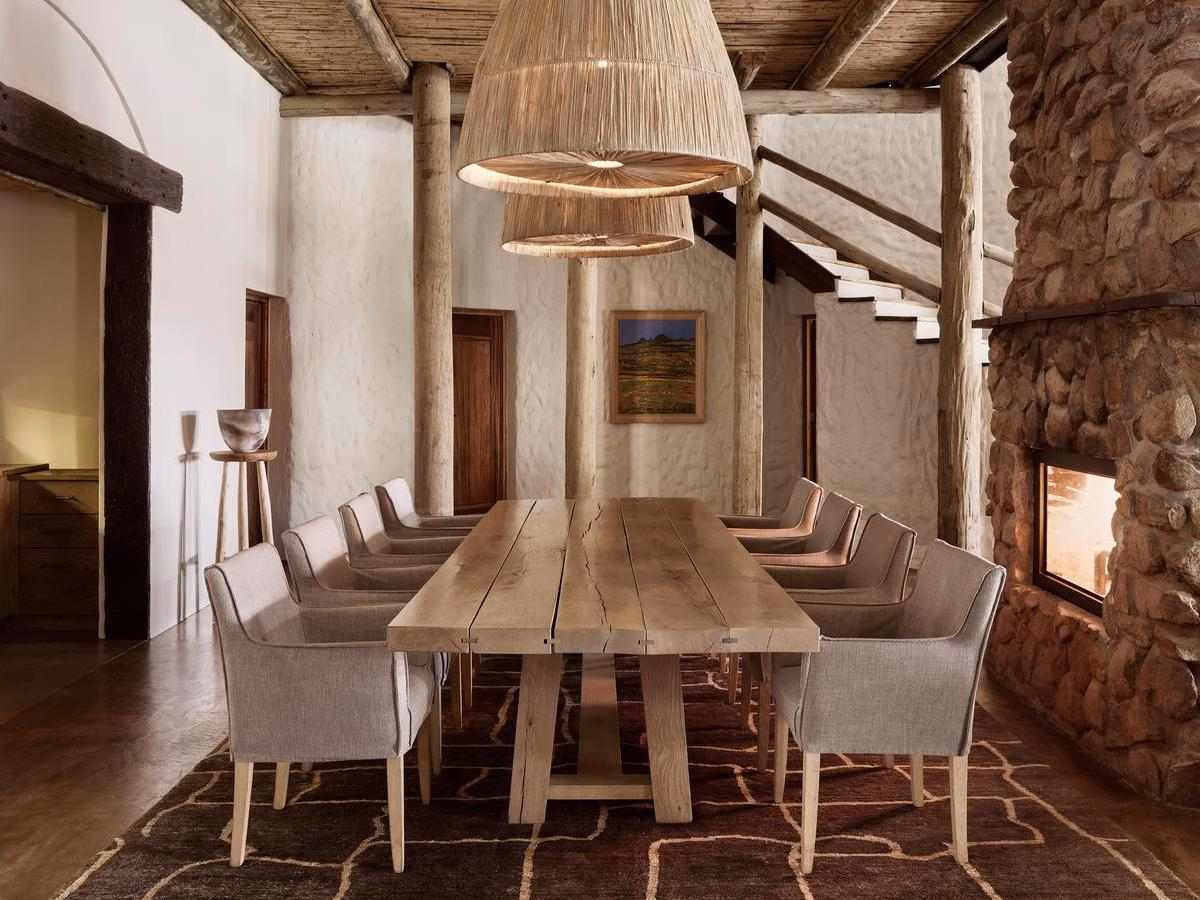A spacious indoor dining room with a wooden table, stone fireplace, and woven pendant lamps.