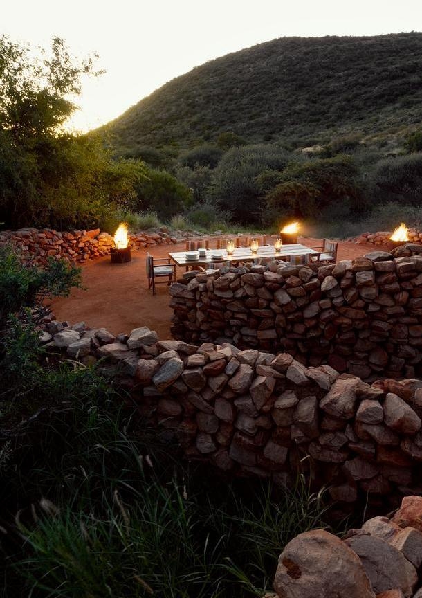 A set outdoor dining table inside a stone boma with small fires burning along the perimeter.