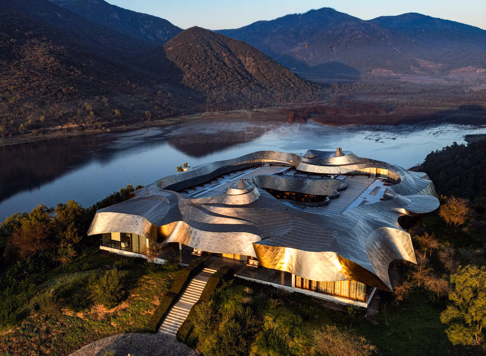 Aerial view of Vik Chile showing a modern building with a flowing silver metal roof overlooking a lake and mountains.