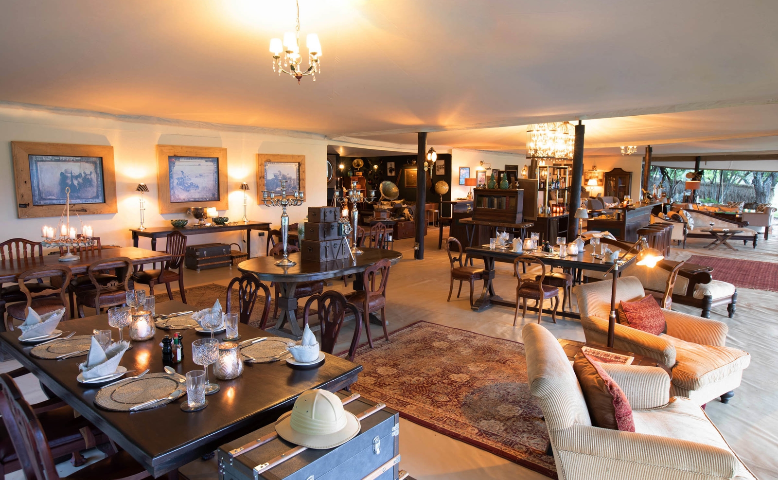 Interior of a large canvas dining tent with set tables, vintage decor, trunks, framed pictures, and cozy lounge seating areas.