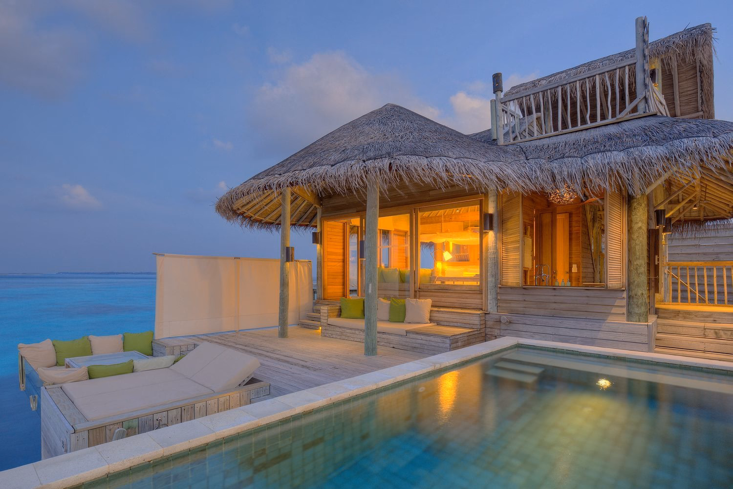 Overwater villa lit up at dusk at Six Senses Laamu