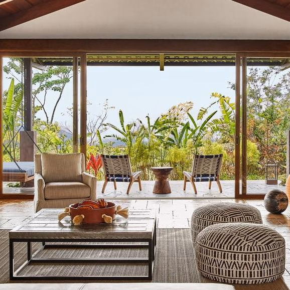 Modern living room of one of Hacienda AltaGracia's casitas with woven furniture and large glass doors overlooking a tropical forest and mountains.