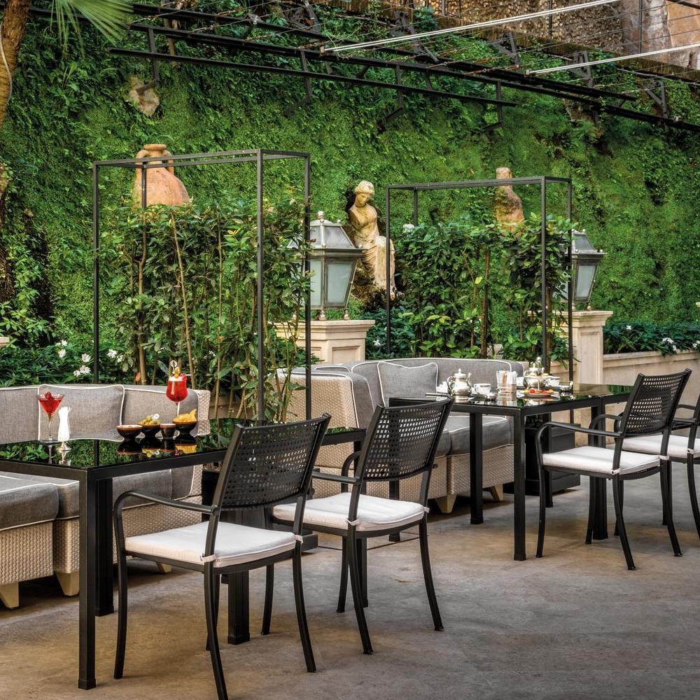 Outdoor restaurant terrace with tables, chairs and rattan sofas. The wall is covered in ivy and has statues and lanterns.