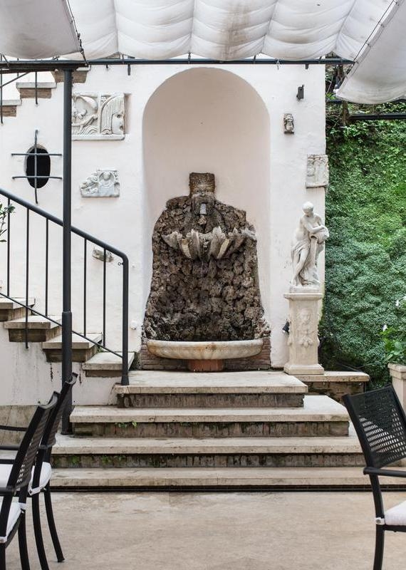 Stone wall fountain and classical statue in an outdoor seating courtyard at the Hassler Roma hotel.