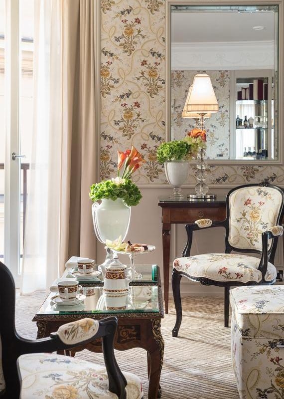 Elegant tea seating area with floral armchairs, a mirrored coffee table, and patterned wallpaper at Hassler Roma hotel.