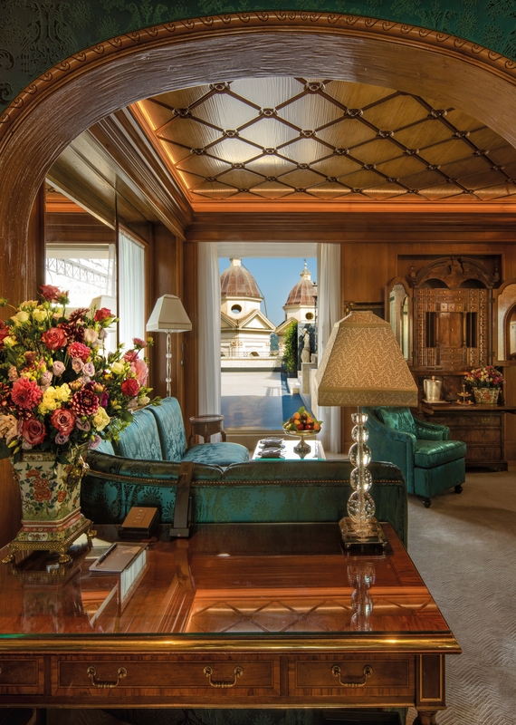 Living room at Hassler Roma hotel with green couches, a wooden desk, and a balcony viewing historic domes.
