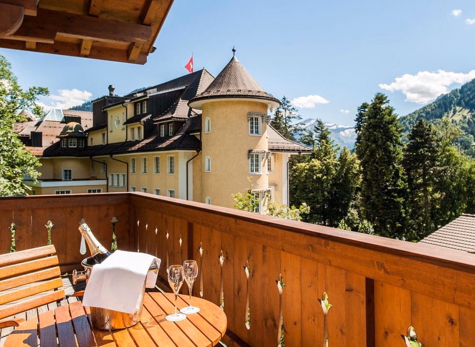 Champagne on a wooden balcony at Le Grand Bellevue with a view of the hotel towers and Swiss mountains.