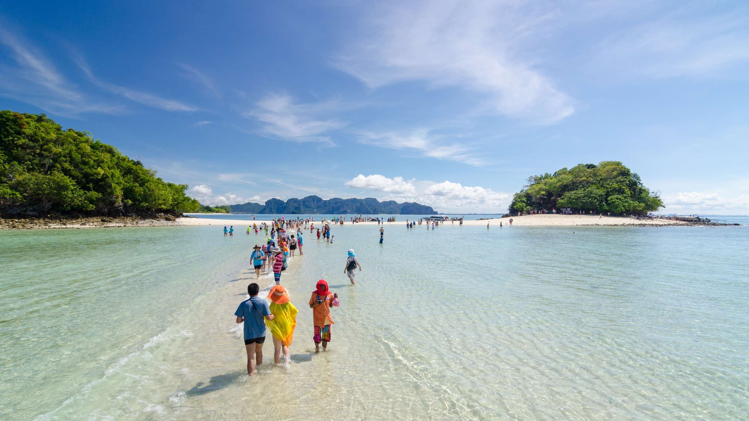 Families wading through shllow clear sea water on a golden sand bank