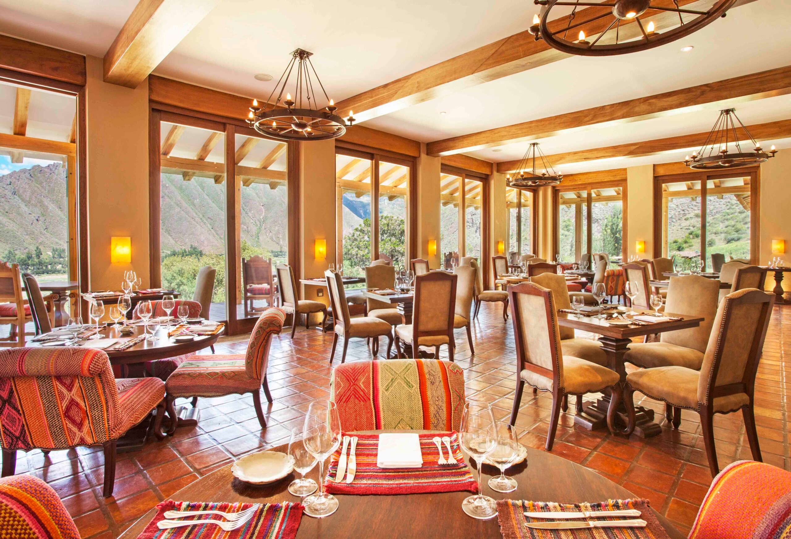 Elegant dining room with large windows, mountain views, wooden beams, and patterned textiles.