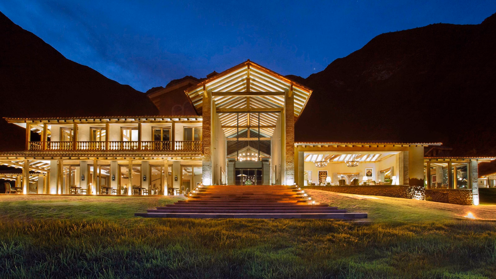 Illuminated two-story building at dusk with large front steps and mountain backdrop.