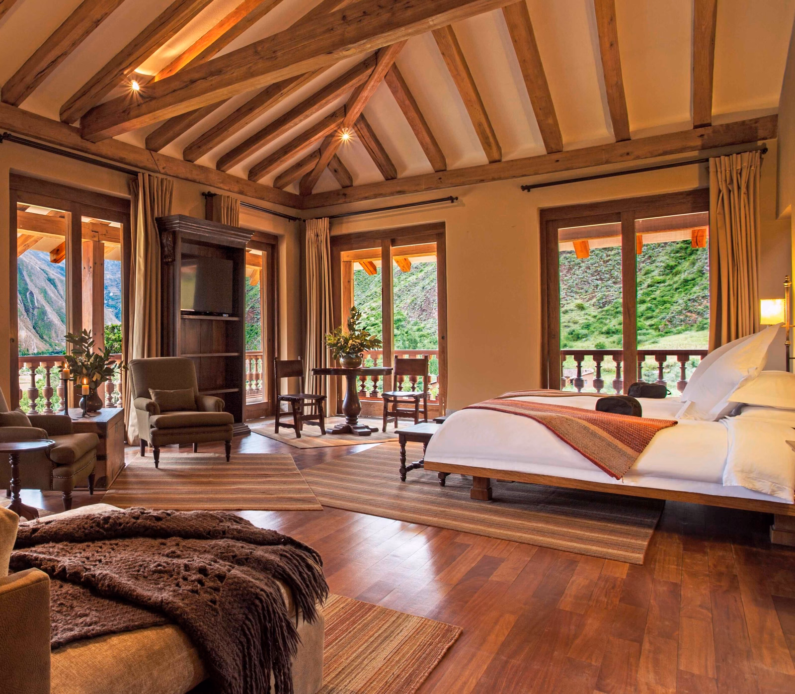 Luxurious bedroom with wooden beams, plush bed, and mountain view through open balcony doors.