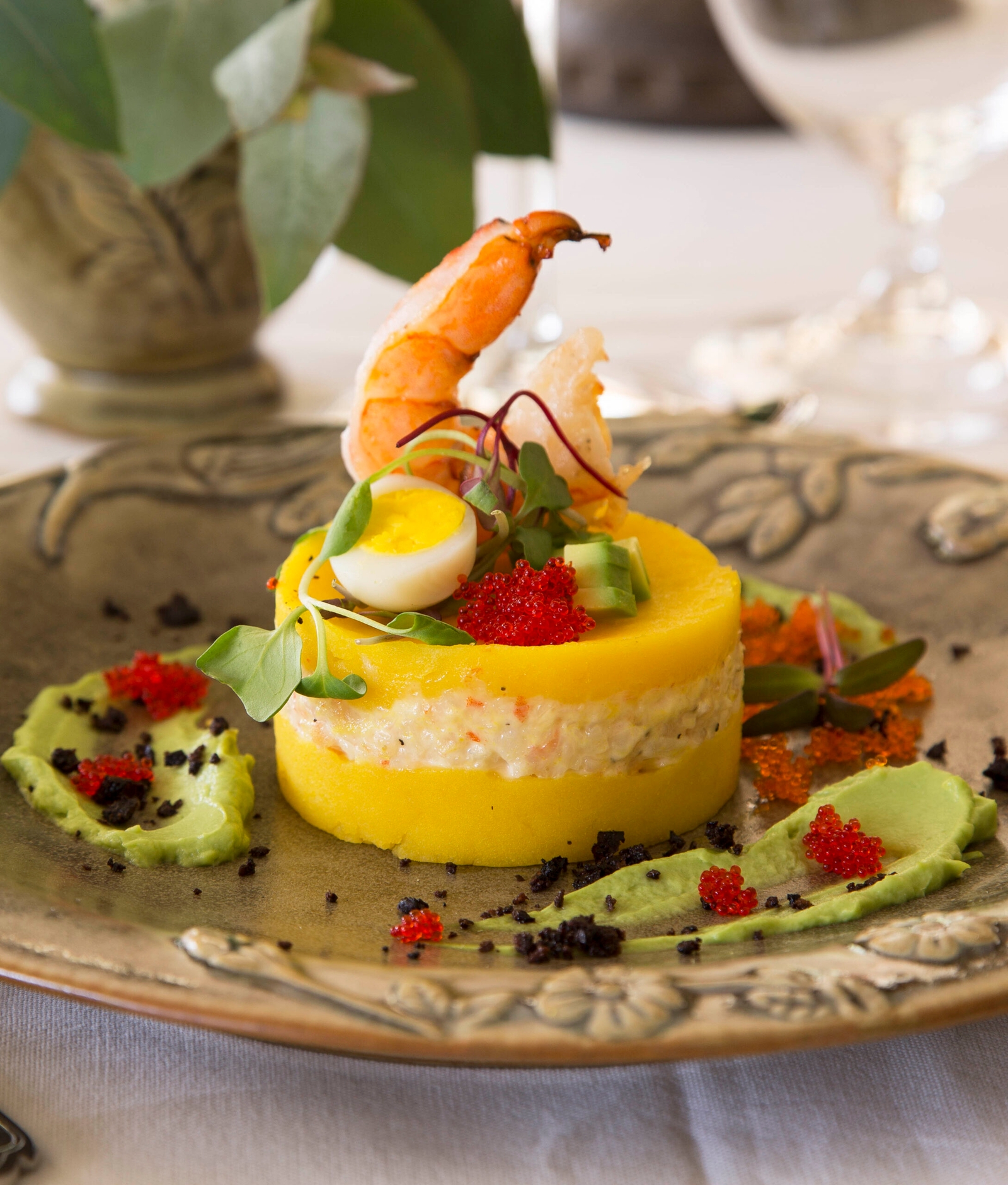 A gourmet dish with layers of yellow polenta, crab salad, shrimp, roe, and a quail egg.