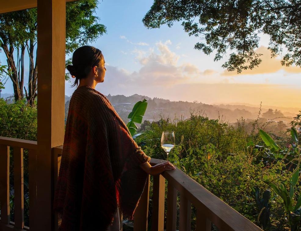 A woman on a balcony overlooking dense greenery.