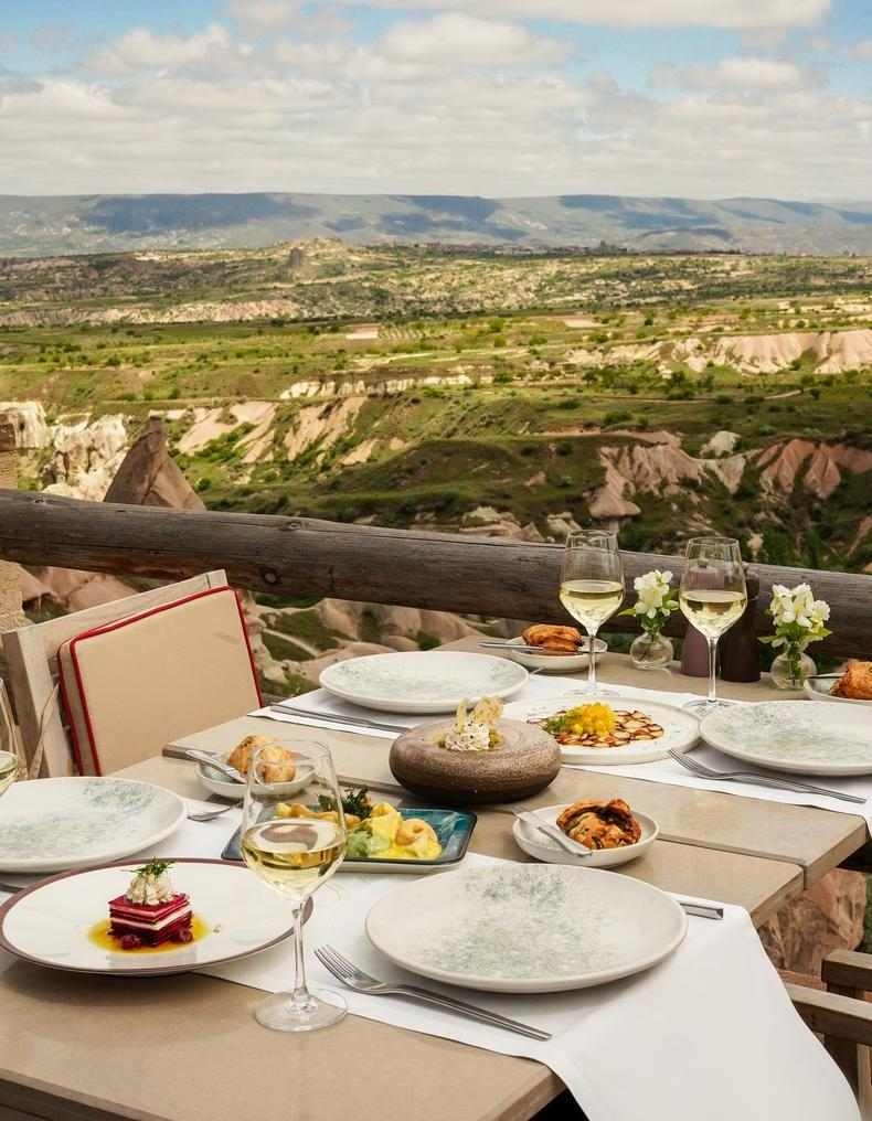 A gourmet dinner spread with wine glasses on a terrace overlooking a scenic mountain valley.
