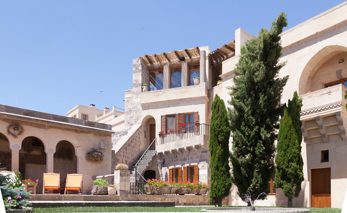 A traditional stone building with balconies, stairs and cypress trees under a clear blue sky.