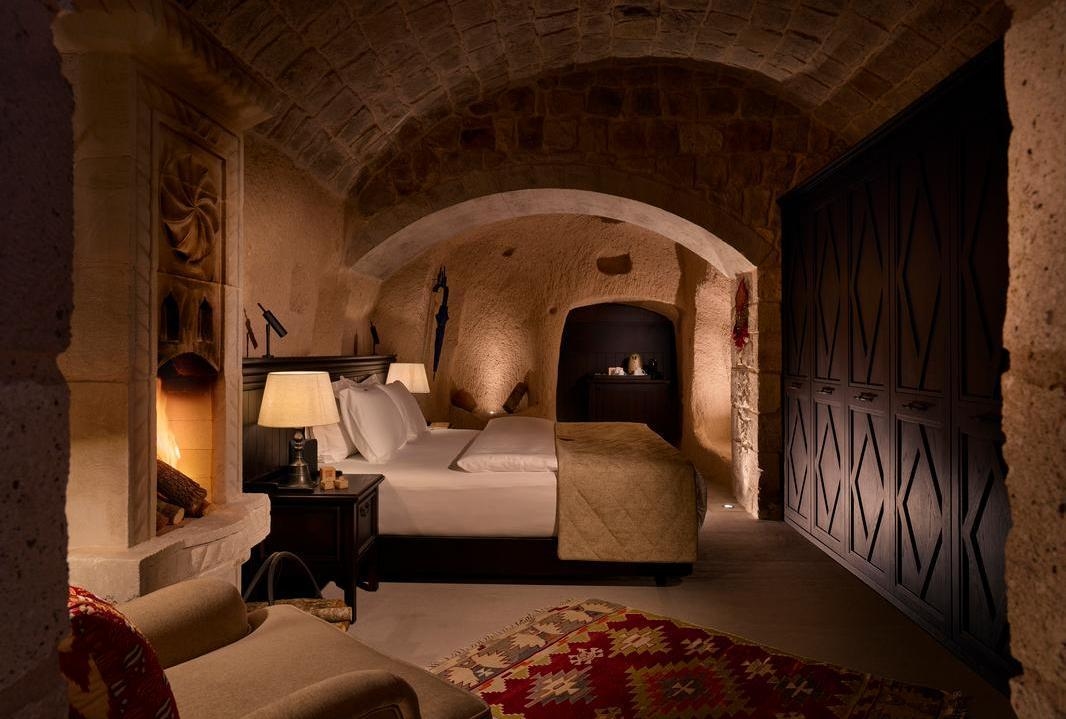 A cosy cave bedroom with a stone fireplace, arched ceilings and a large bed.