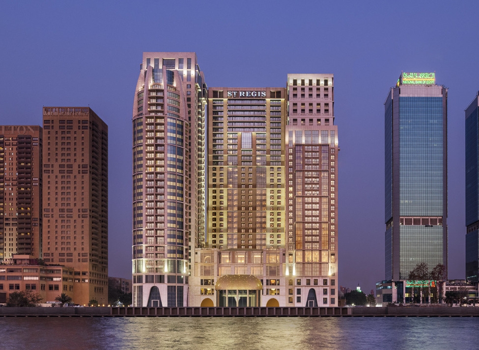 The St. Regis Cairo hotel and neighboring skyscrapers reflecting in the Nile River at dusk under a deep blue sky.