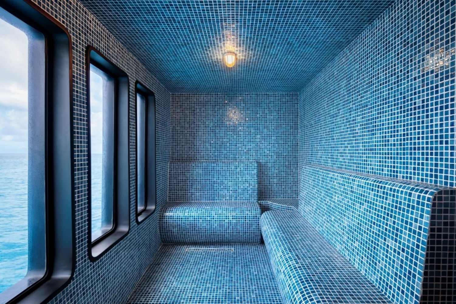 Interior of a blue mosaic-tiled hammam with large windows overlooking the ocean.