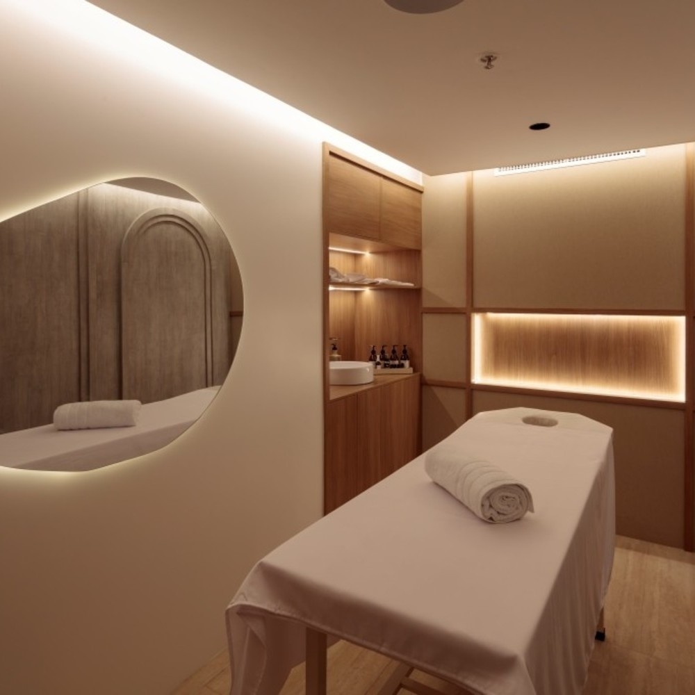Minimalist spa treatment room on the Hermes catamaran featuring a prepared massage table and illuminated oval mirror.