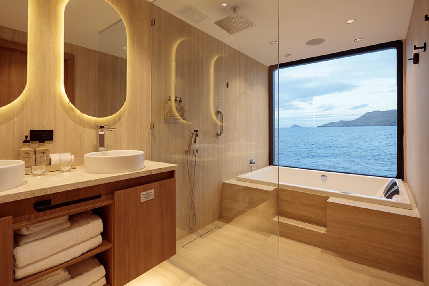 Modern catamaran bathroom featuring a double vanity, glass shower, and bathtub beside a large ocean-view window.