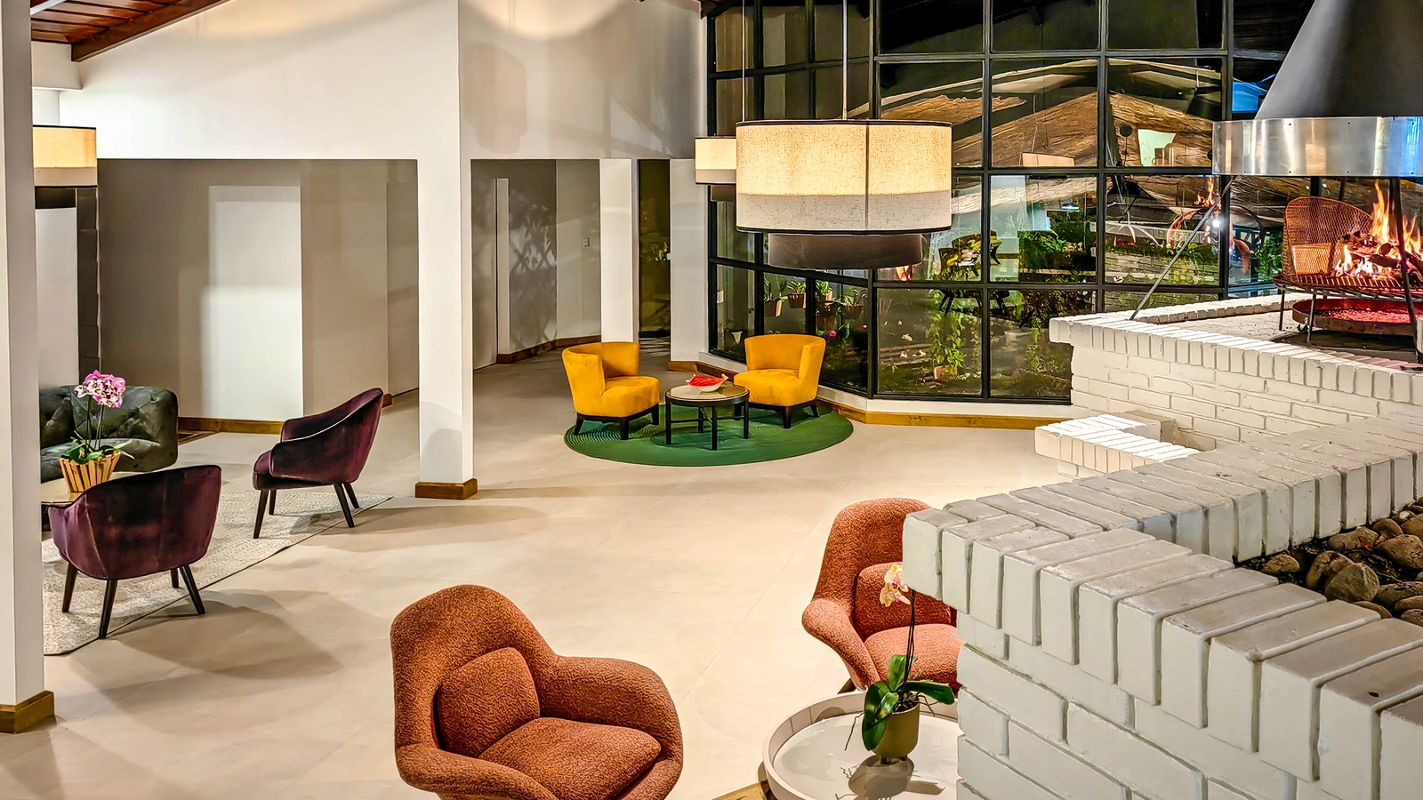 A modern lounge at Monteverde Lodge with a brick fireplace, yellow and purple chairs, and large glass windows.