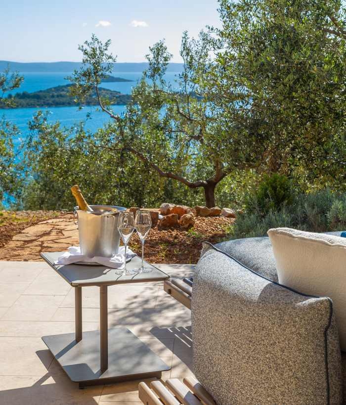 Champagne in an ice bucket on a small table by an outdoor sofa with a scenic view of the sea.