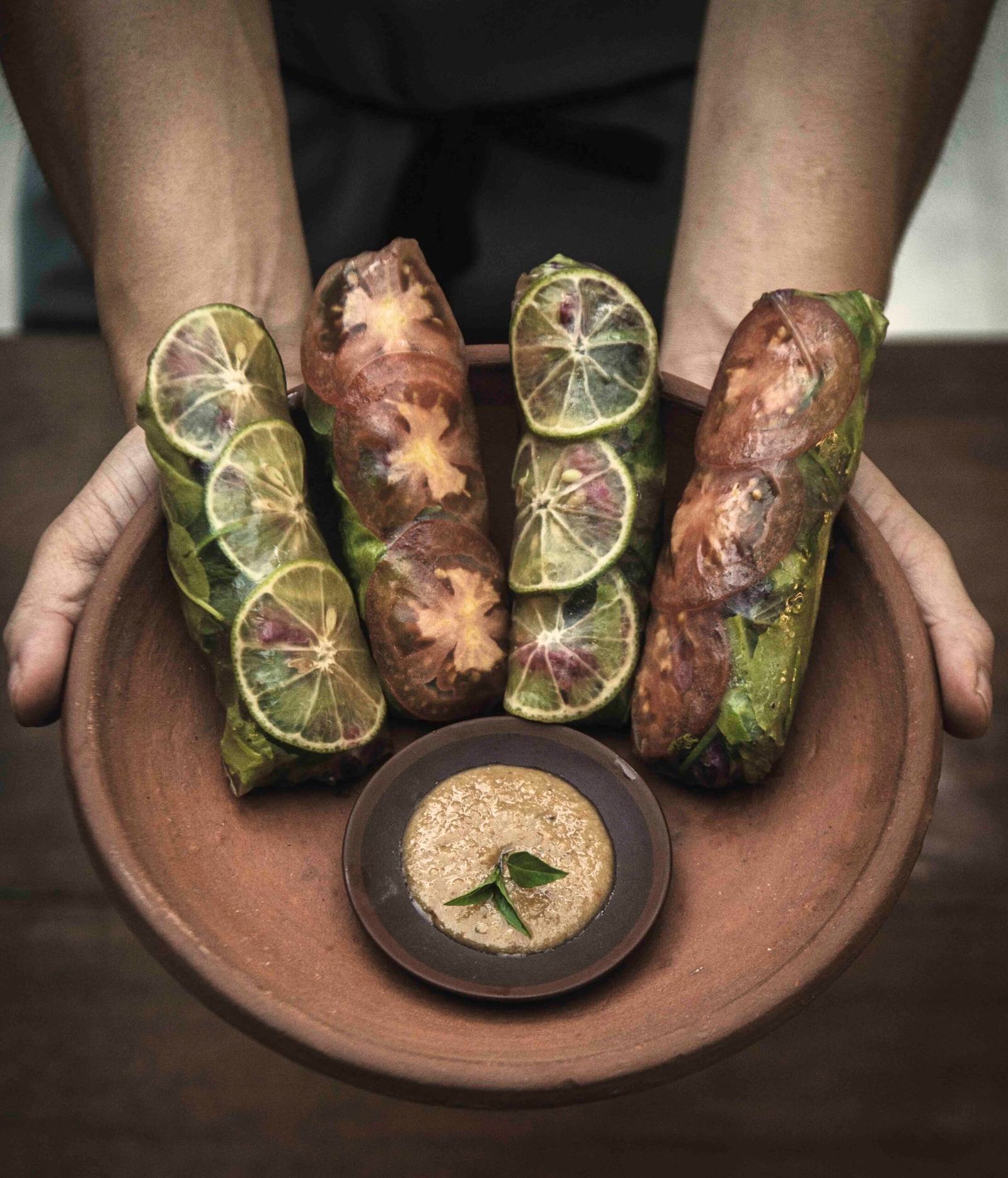 Close up of hands holding out a terracotta bowl with leaf-wrapped food