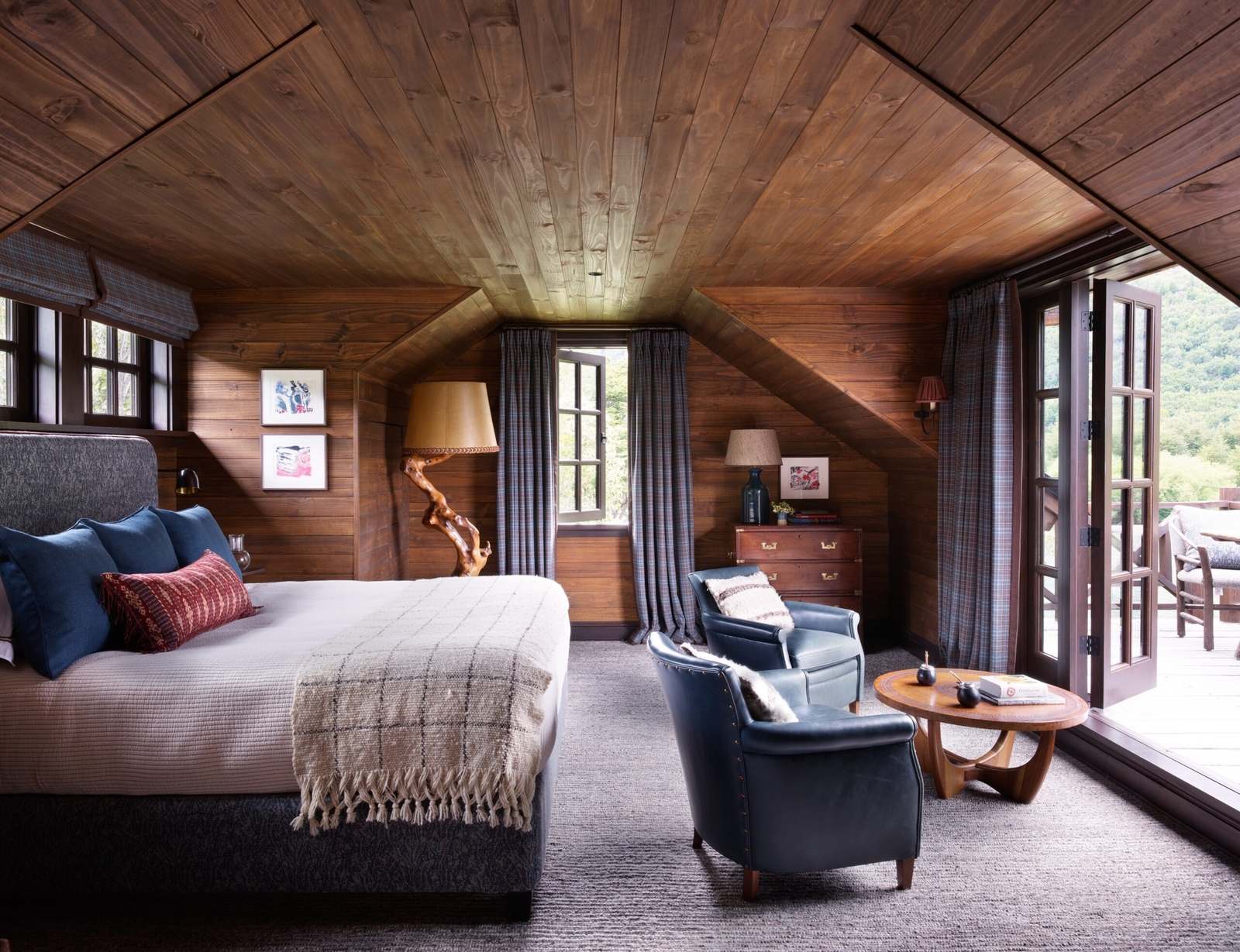Cozy wooden cabin bedroom with a bed, armchairs, and balcony access.