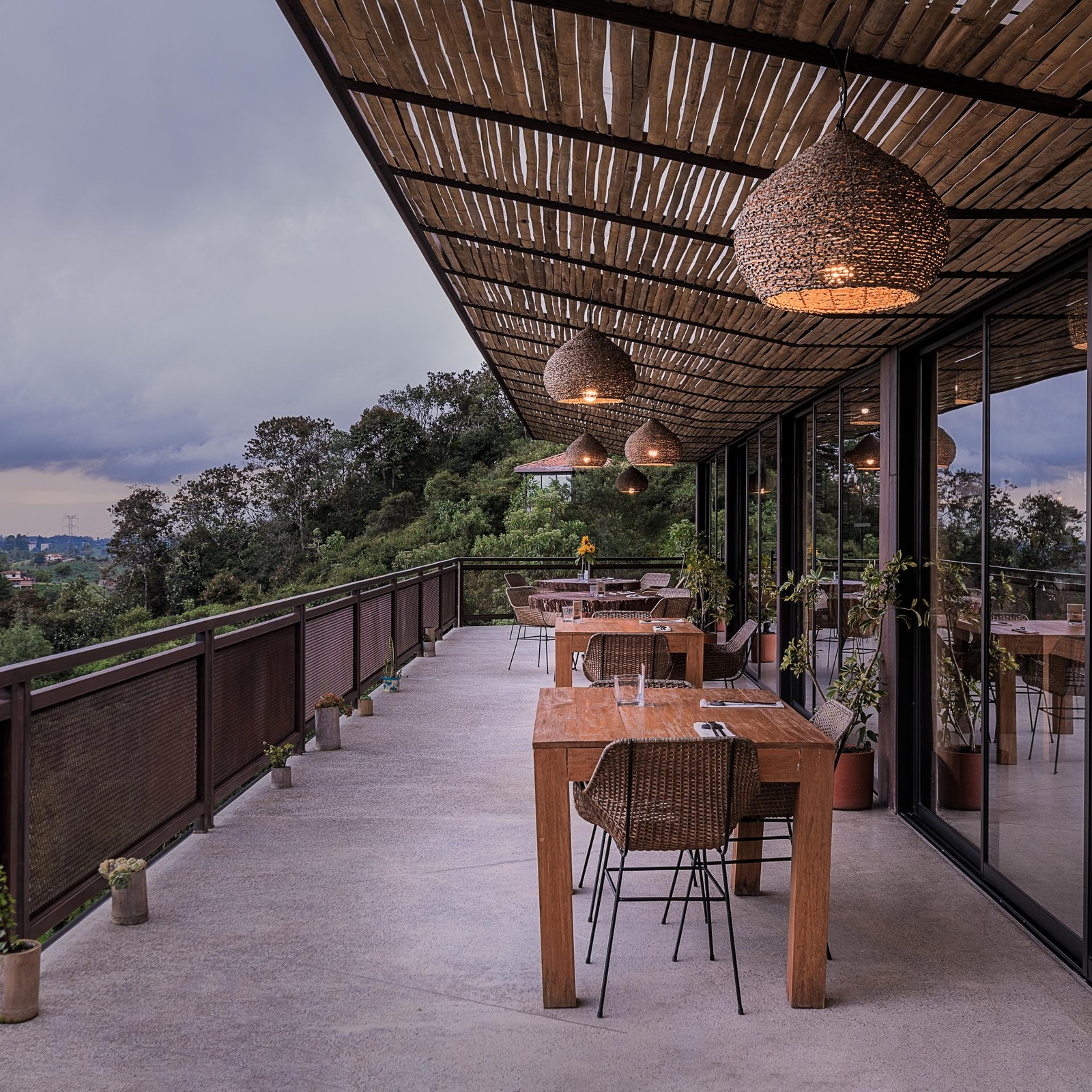 Terrace dining area with wooden furniture and hanging basket lamps overlooking a treed landscape.