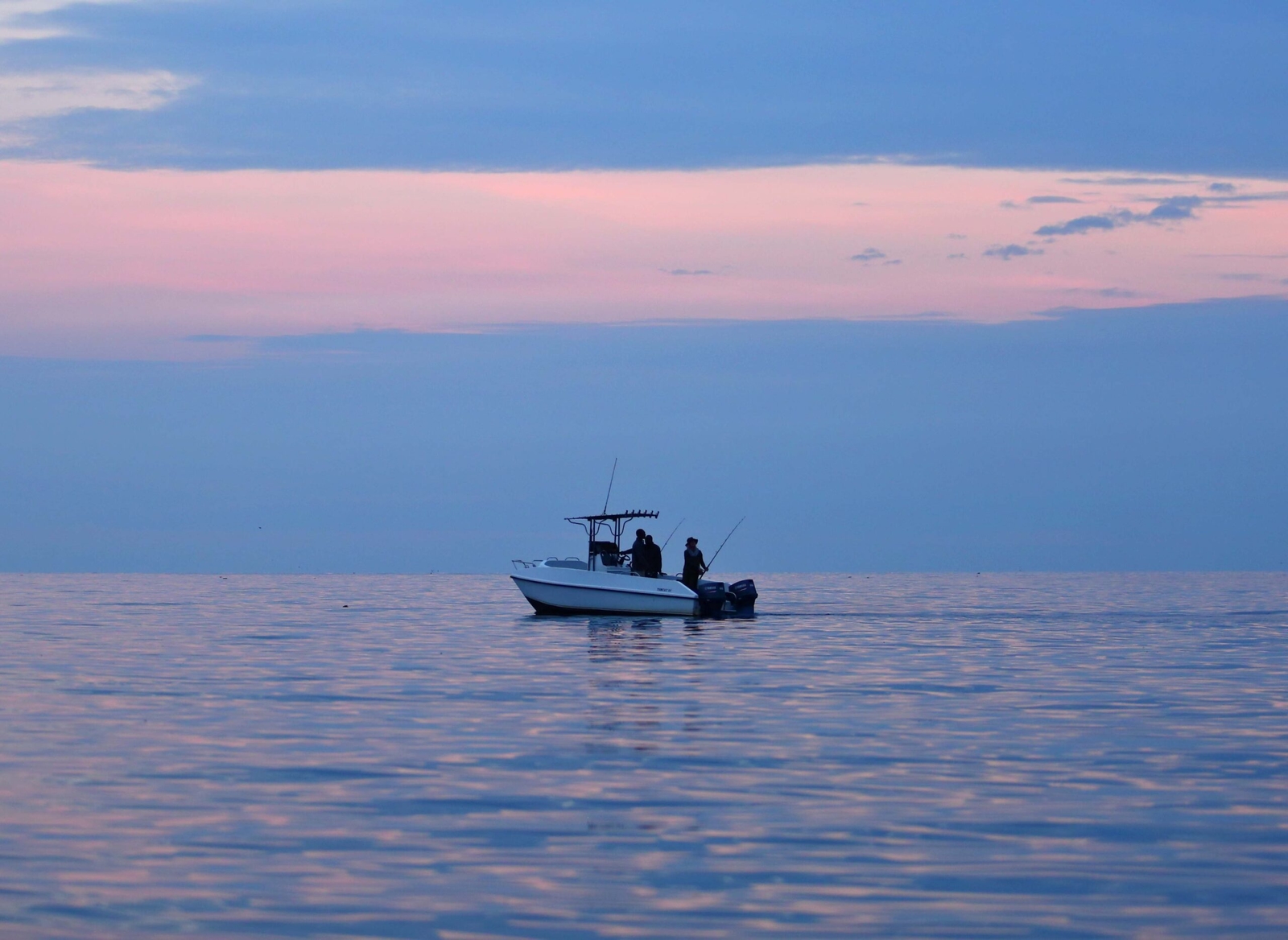 A boat with people fishing on calm water during twilight.