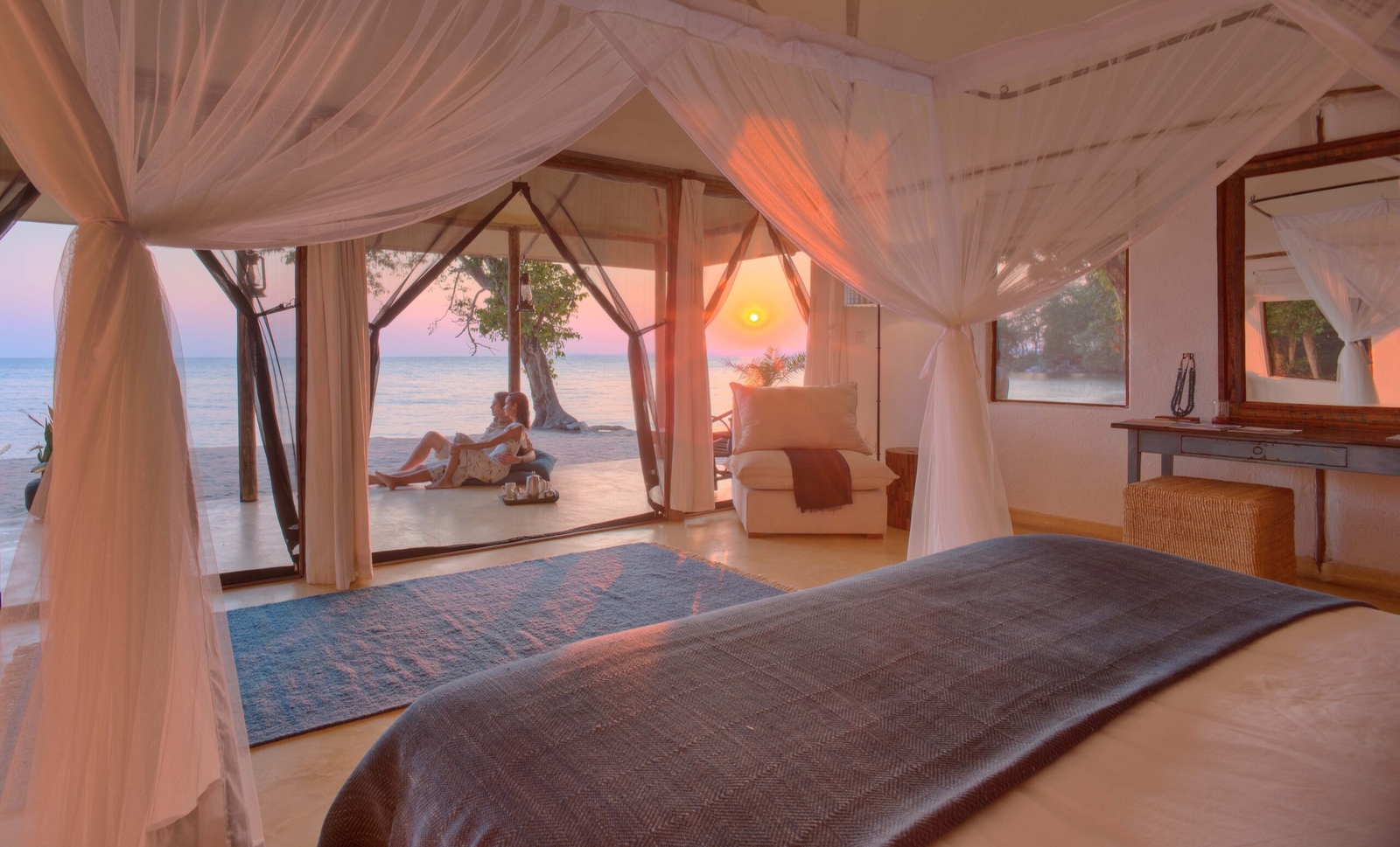 Beachfront room with open doors, a person relaxing, and a sunset view.