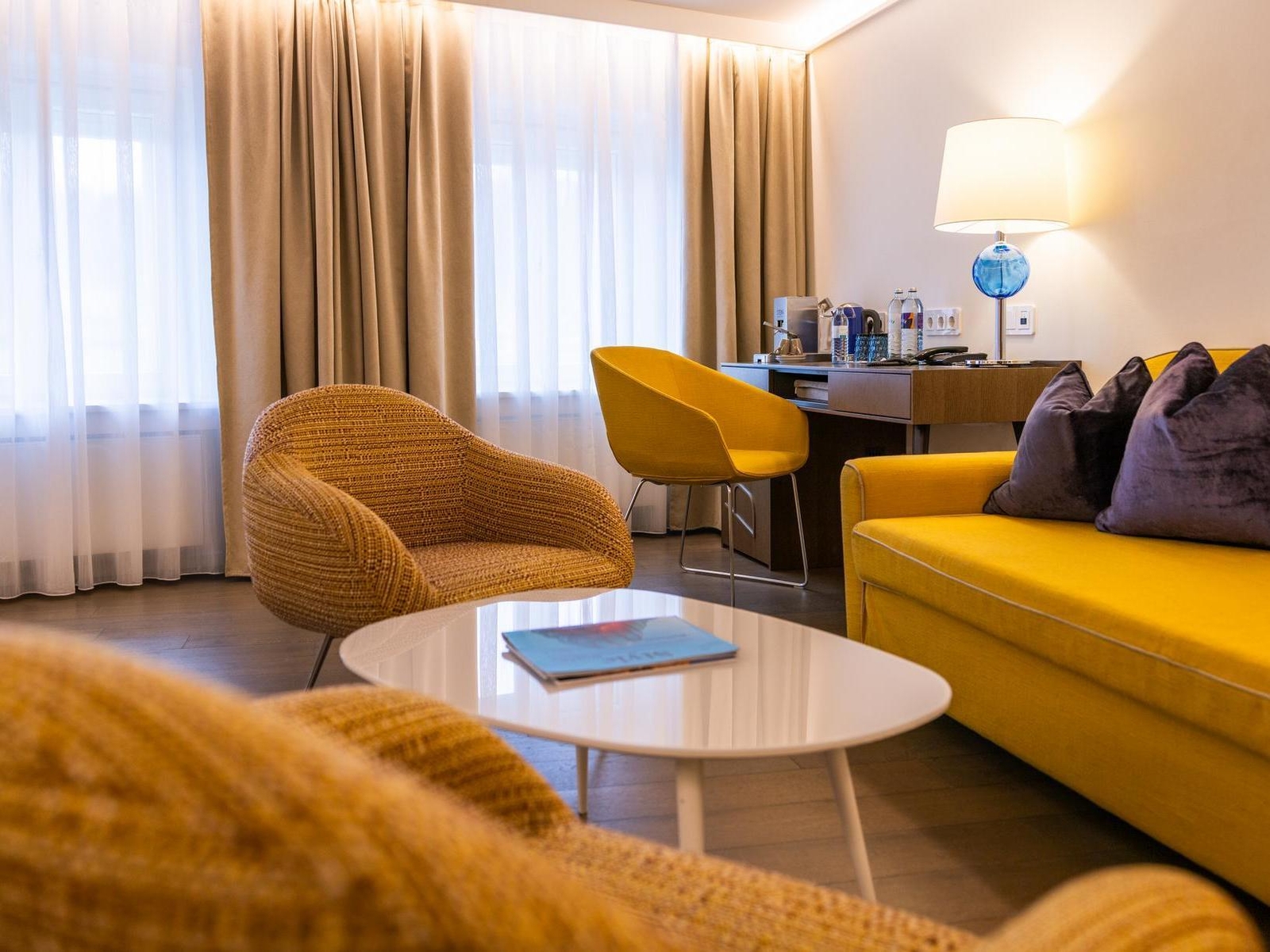 Modern living room with a yellow sofa, rattan chair, and white coffee table.