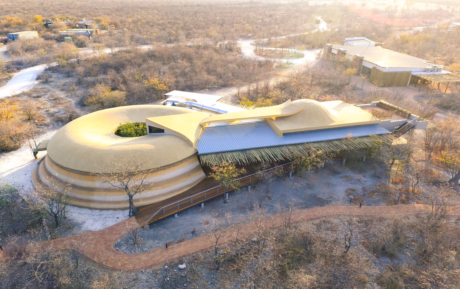 Aerial view of a unique circular building with a green roof in a dry landscape.