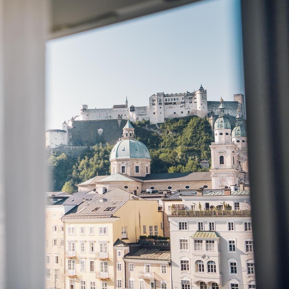 View of a historic fortress above European-style buildings, seen through an open window.