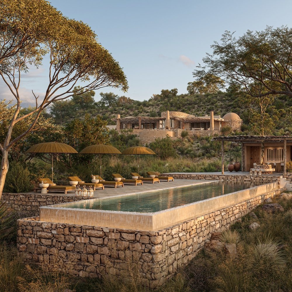 A luxury rustic-style villa with an infinity pool surrounded by nature and lounge chairs under umbrellas.