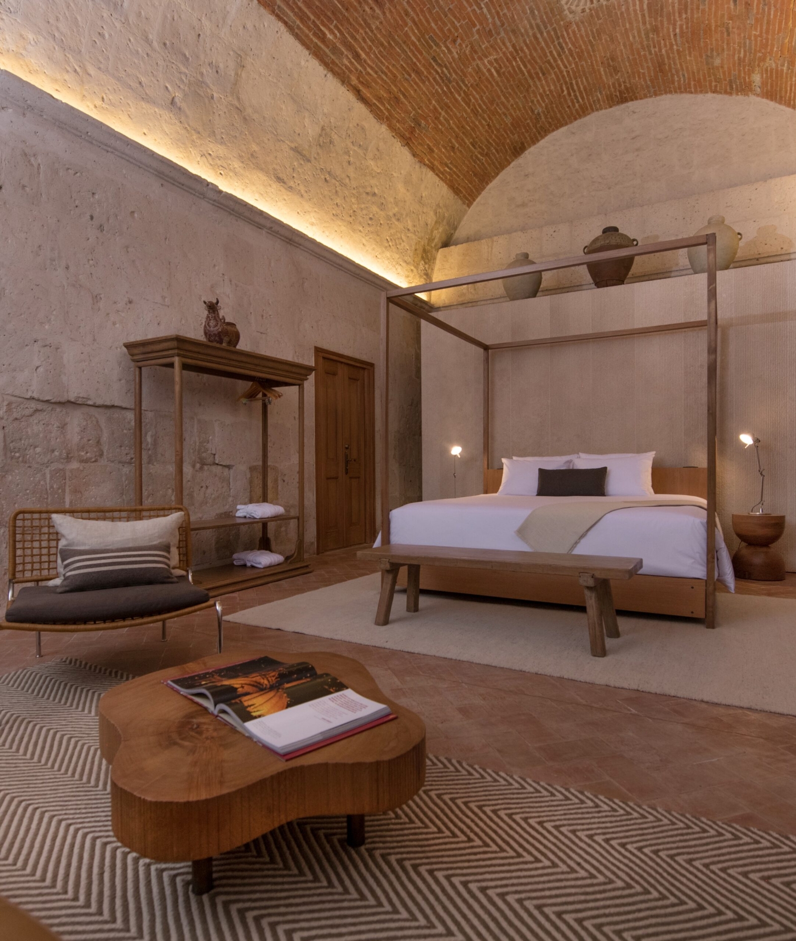 Rustic bedroom with a canopy bed, brick ceiling, wooden furniture, and patterned rug.