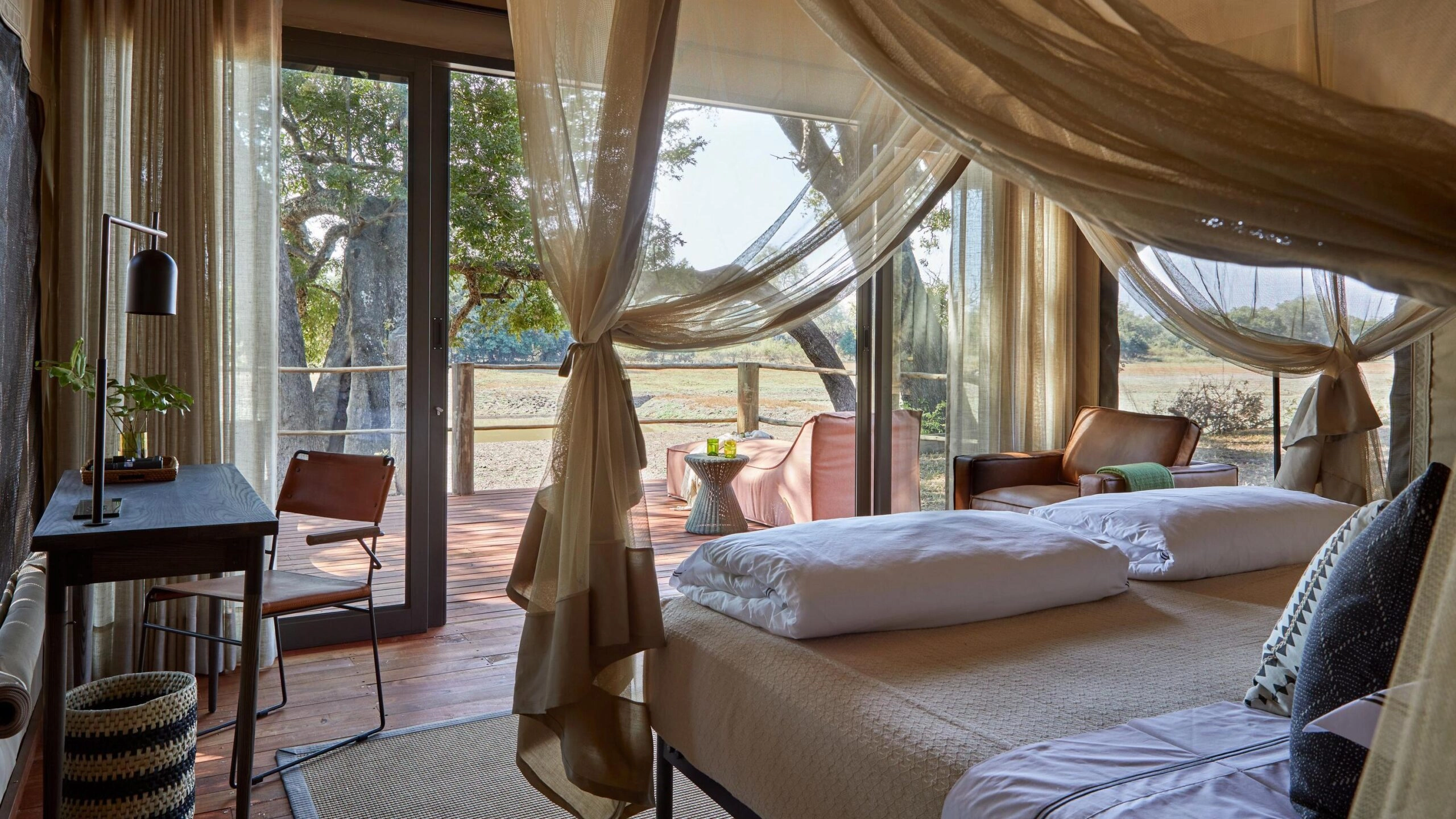 Luxurious safari lodge room with bed, gauzy curtains, and outdoor view.