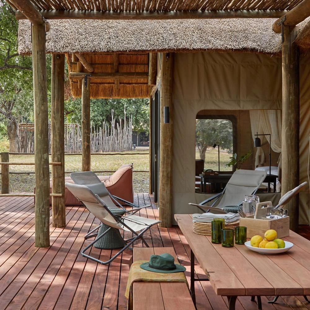 Outdoor safari tent dining area with wooden deck, thatched roof, and relaxed seating.