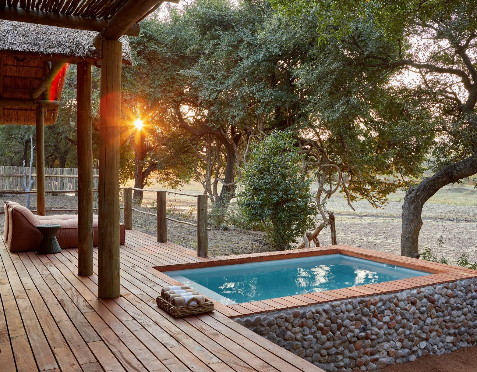 Rustic wooden deck with pool at sunset, surrounded by trees.