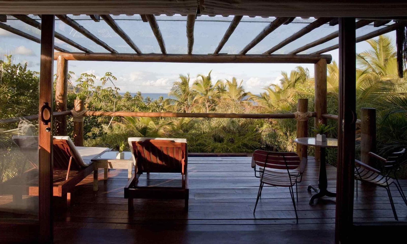 A serene balcony overlooking lush greenery and ocean views, featuring wooden lounge chairs and a small round table.