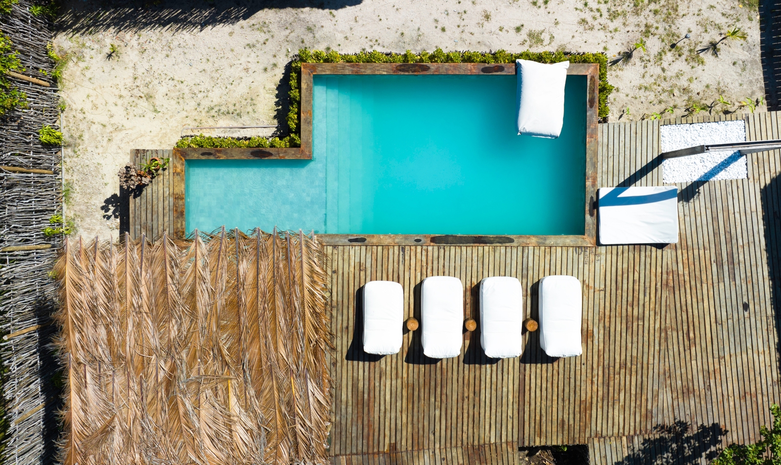On overhead view of a swimming pool with blue water and four white deck chairs and some white towels next to it.